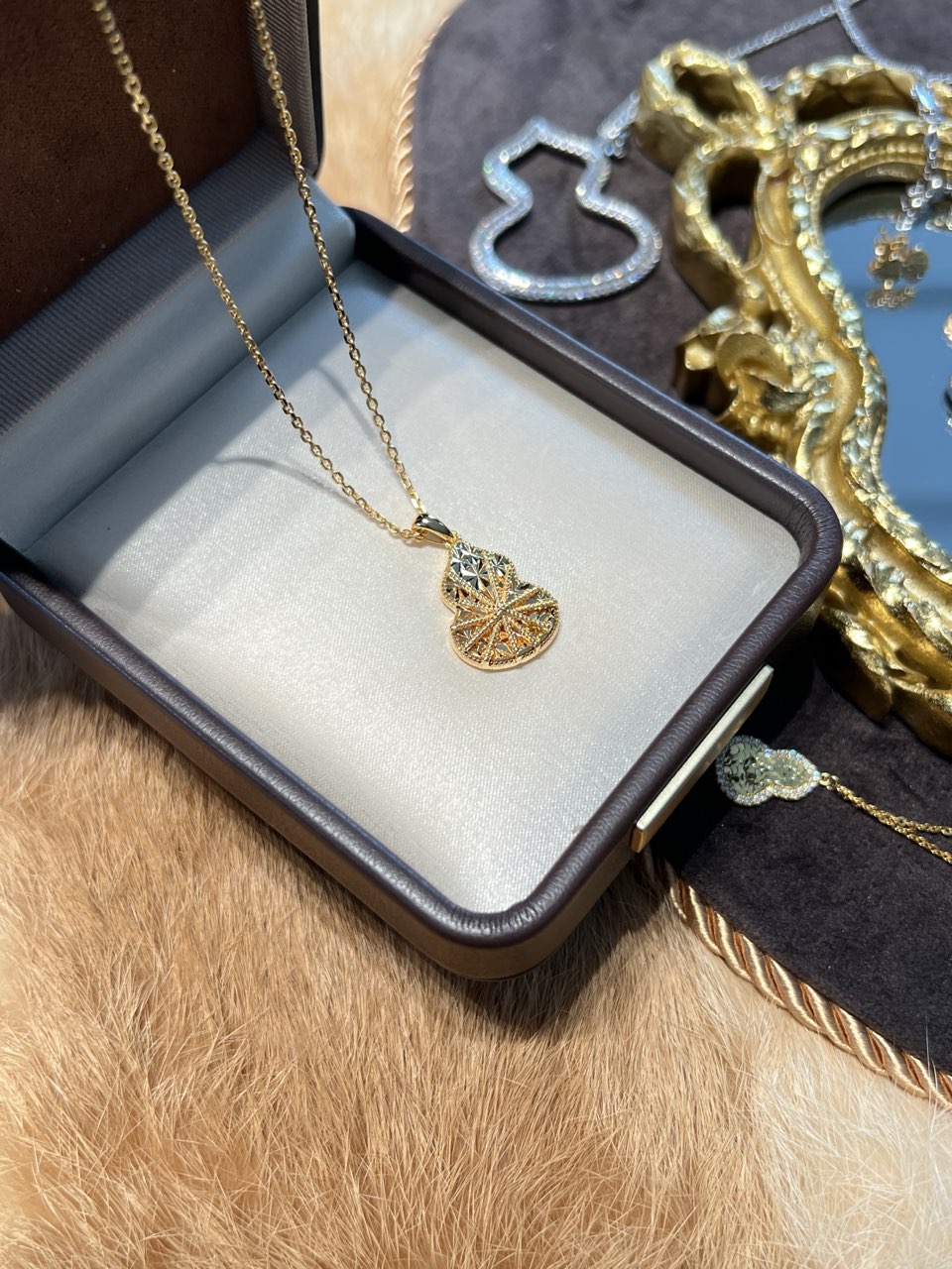 Elysian Jewelry 18k gold-plated 925 silver necklace with a hulu pendant in an open jewelry box on fur.