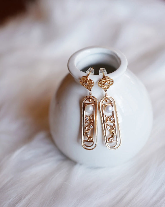 Elysian jewelry 925 silver with 18k gold earrings with pearls on a white ceramic dish against a soft white background