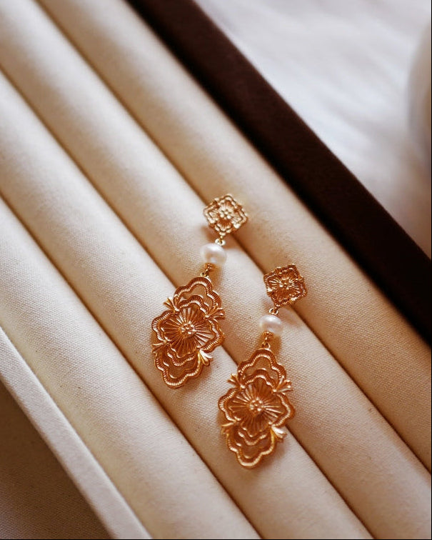 Elysian Jewelry 925 silver with 18k plated gold floral earrings on a white cushion with a yellow flower in the background