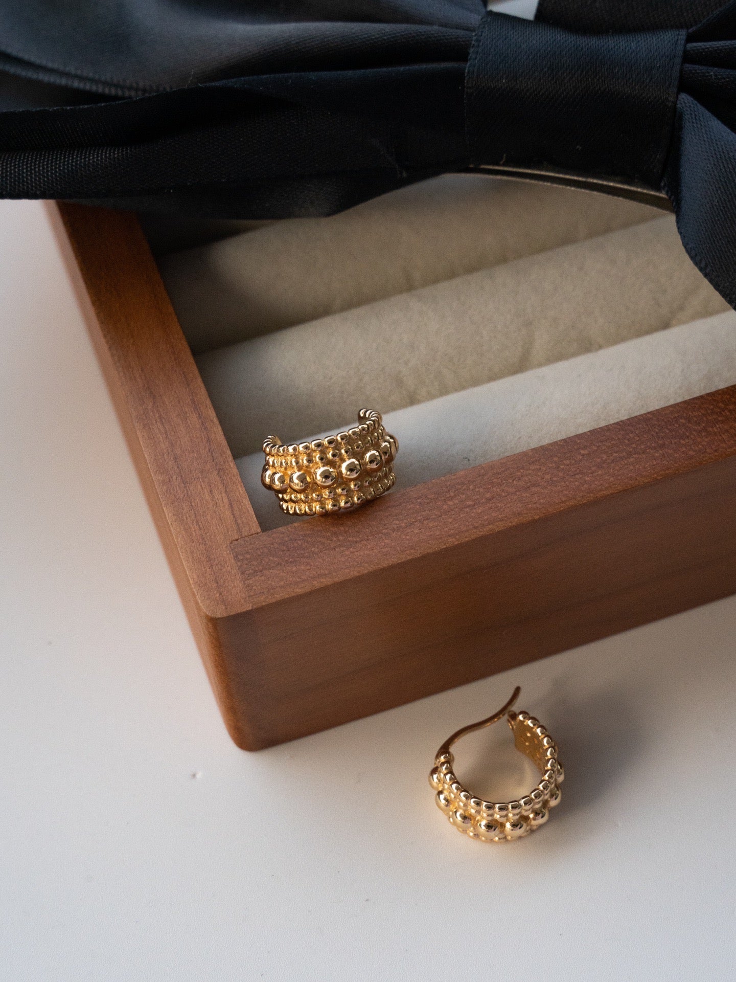 Elysian Jewelry 925 silver with 18k plated gold hoop earrings on a wooden jewelry box with a black bow in the background.