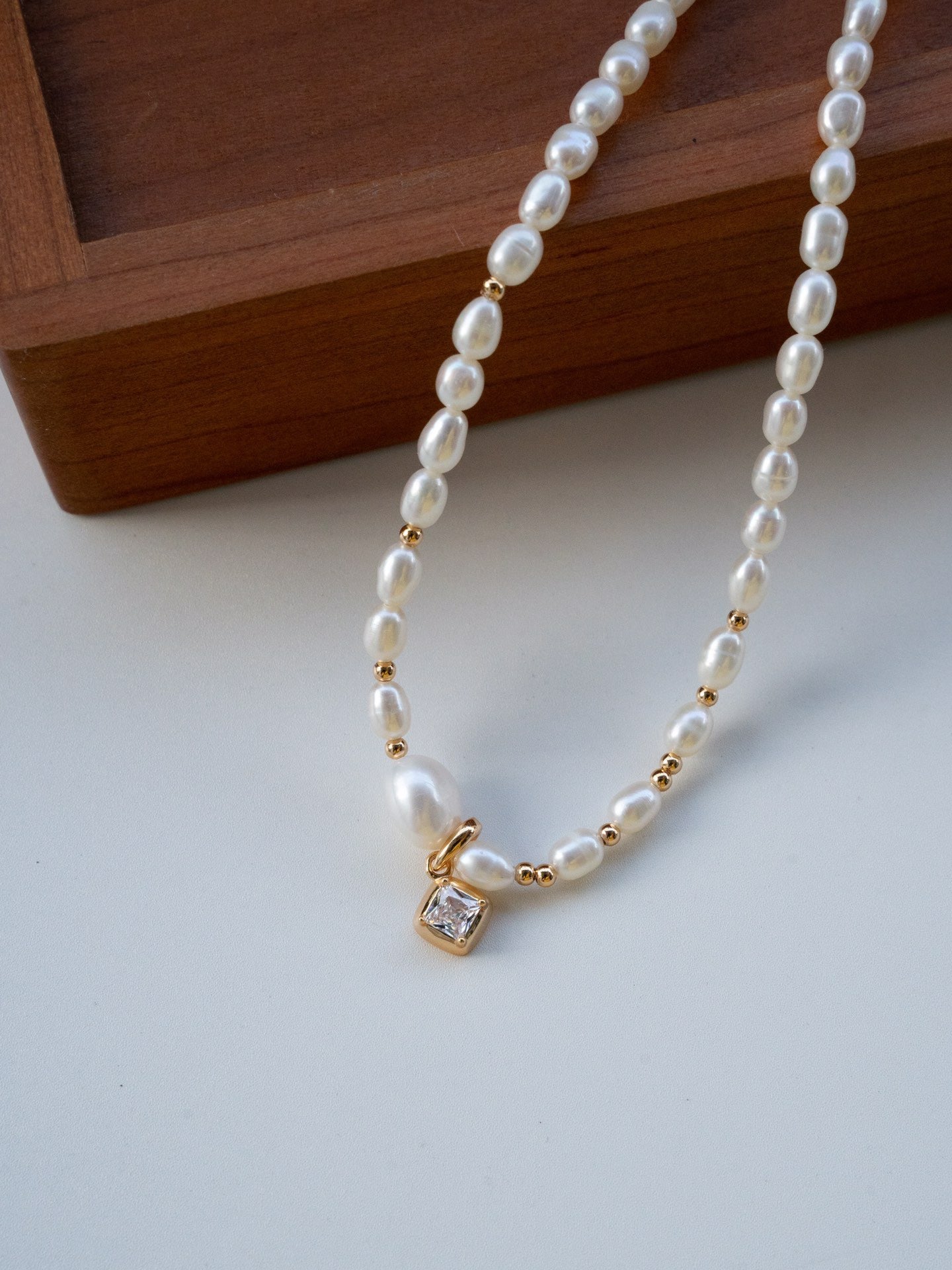Elysian jewelry pearl necklace with a gold clasp on a light surface