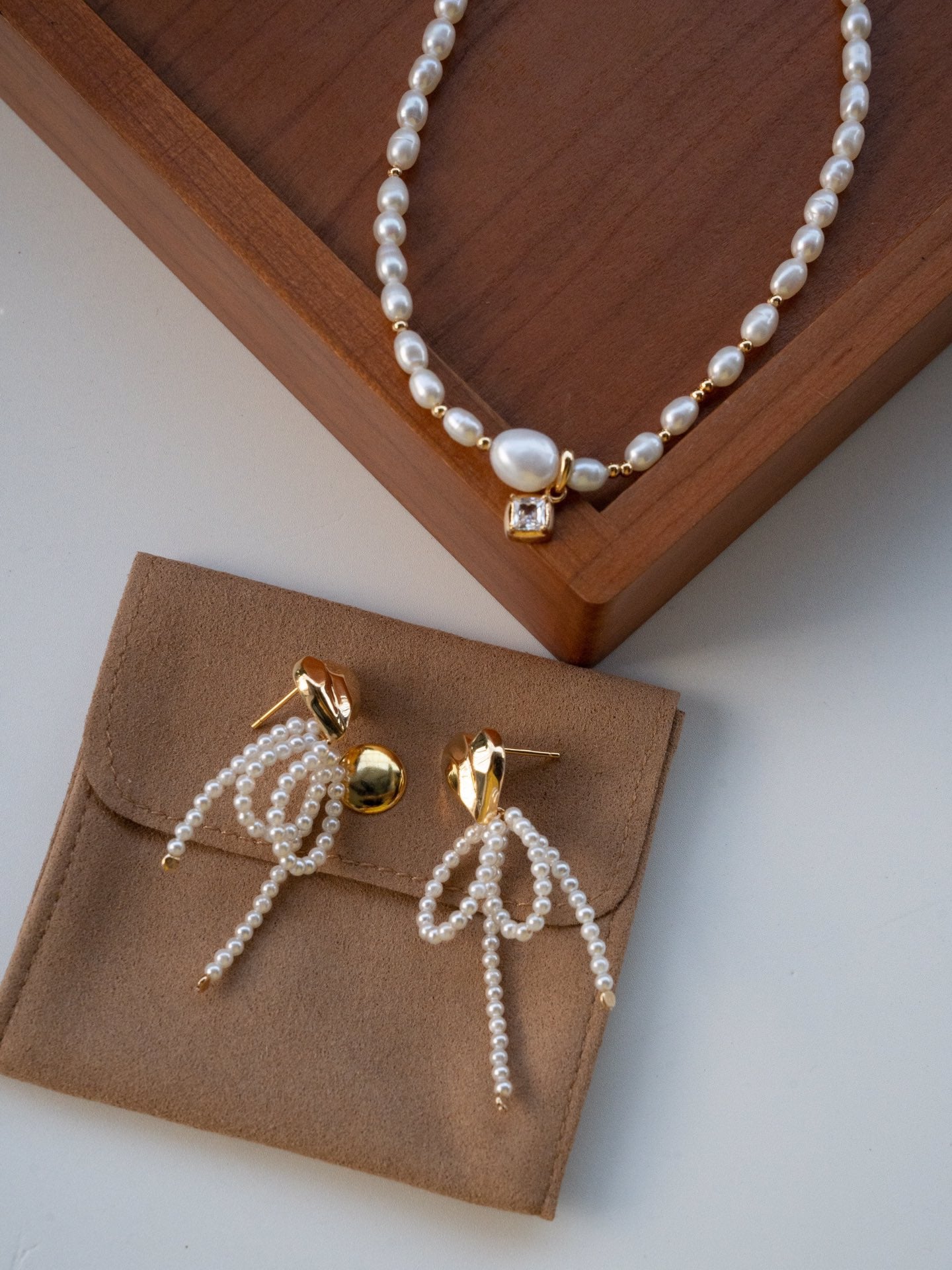 Elysian Jewelry pearl earrings on a brown jewelry pouch with a wooden stand.